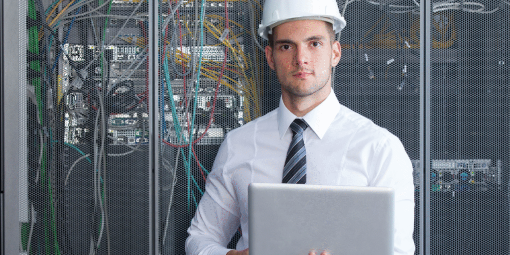 Engenheiro com capacete e notebook em frente a servidores industriais, representando o conceito de justificar investimento em automação para eficiência e controle de processos.